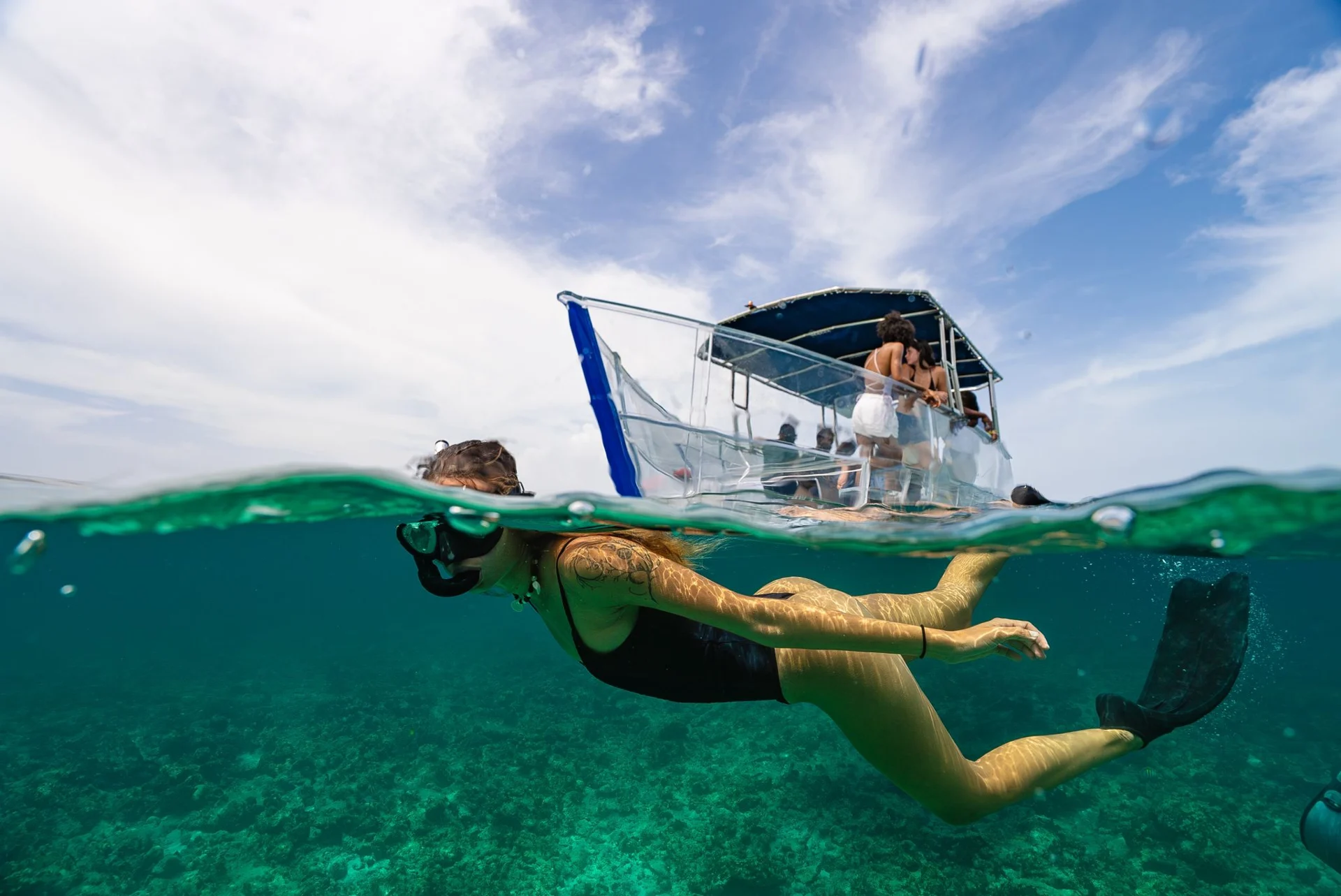 A split-level view of a swimmer and the clear boat above the water