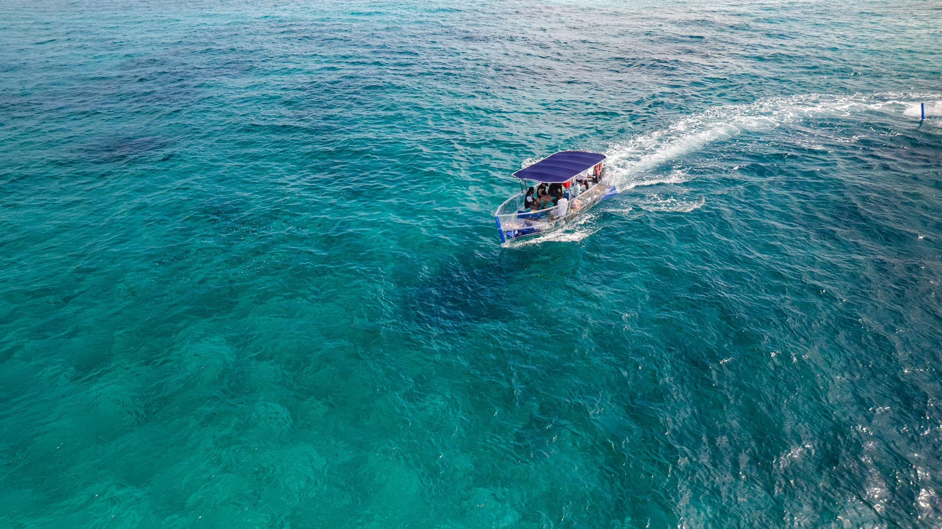 A clear boat gliding through turquoise Bahamian water, seen from above
