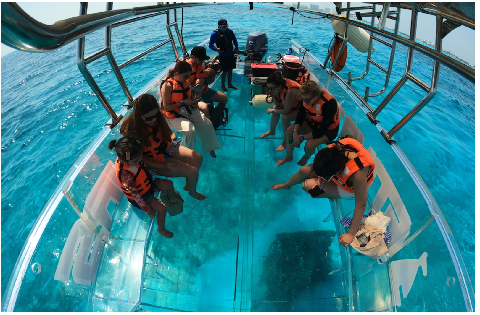 Guests wearing life jackets aboard a clear boat with turquoise water visible through the floor